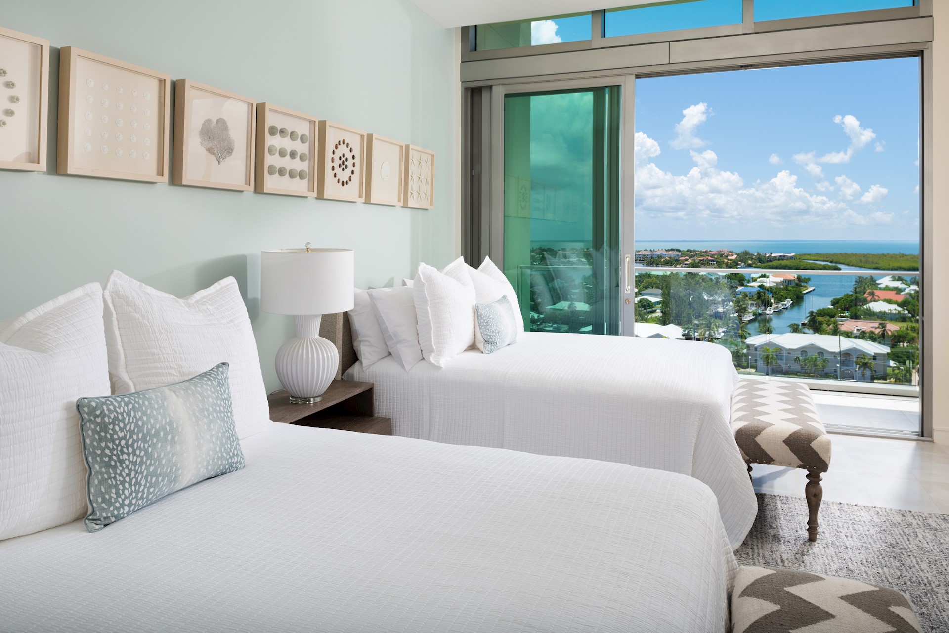 Bedoom with open doors overlooking a canal-front neighborhood. The room has two full sized beds with white duvets and white pillows.