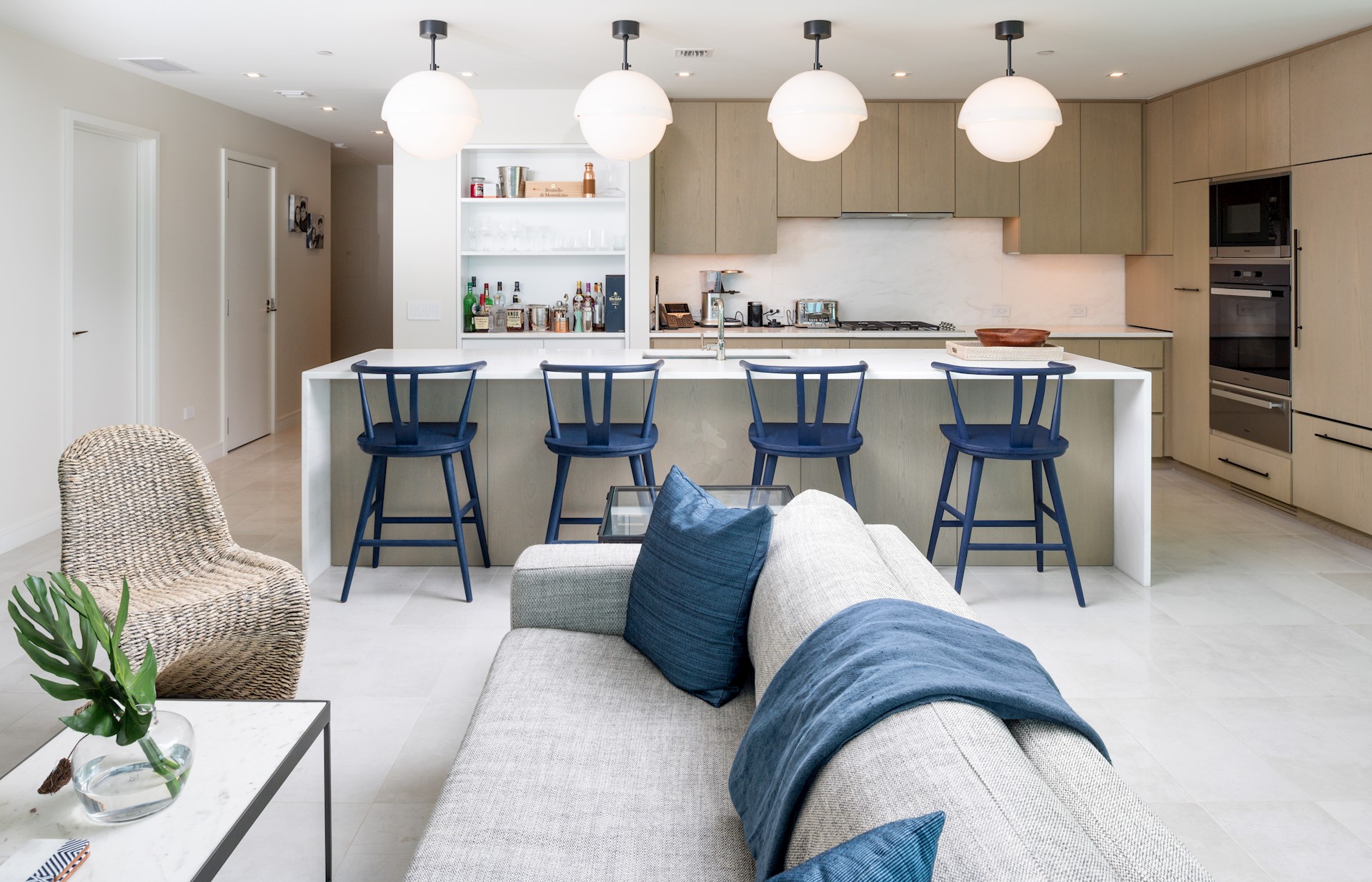 Open plan living room and kitchen with dark blue and tan tones featuring four dark blue stools and four pendant lights over the kitchen island